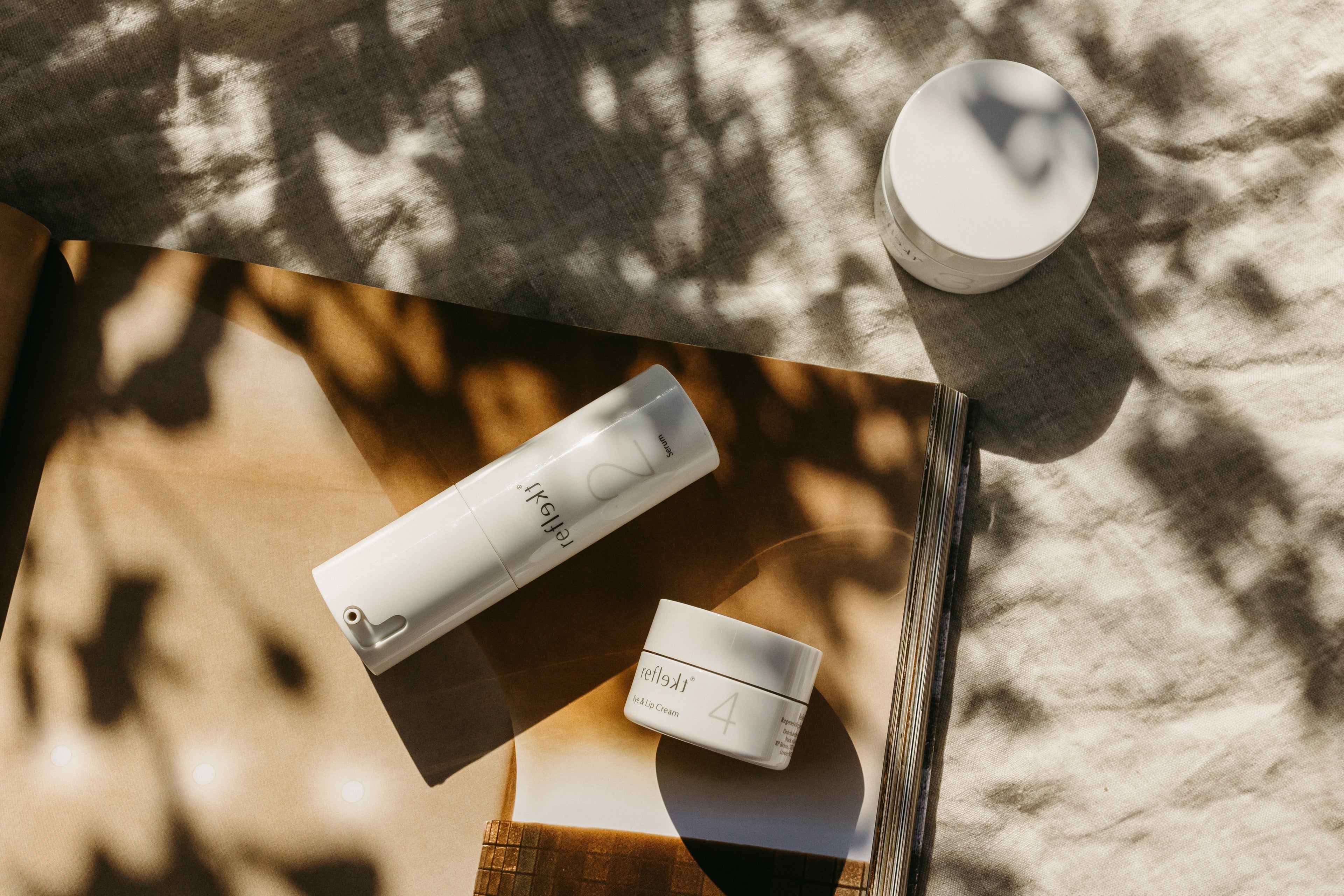 Three Reflekt skincare products displayed outdoors in sunlight on a neutral surface