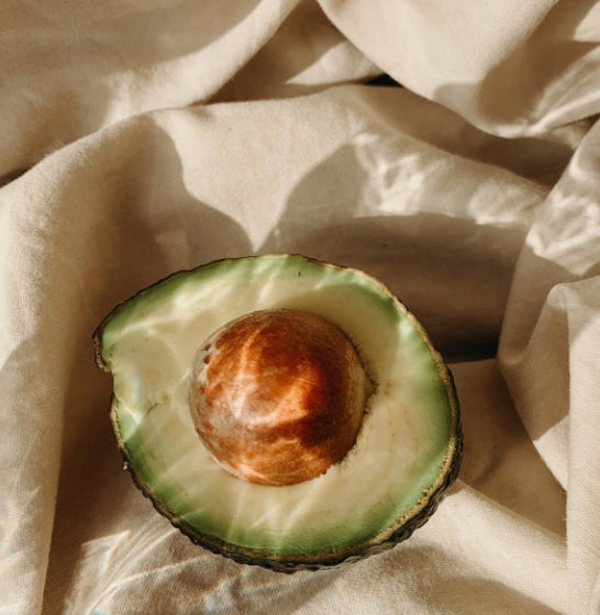 Fresh half avocado resting on soft beige fabric, symbolizing natural ingredients in skincare